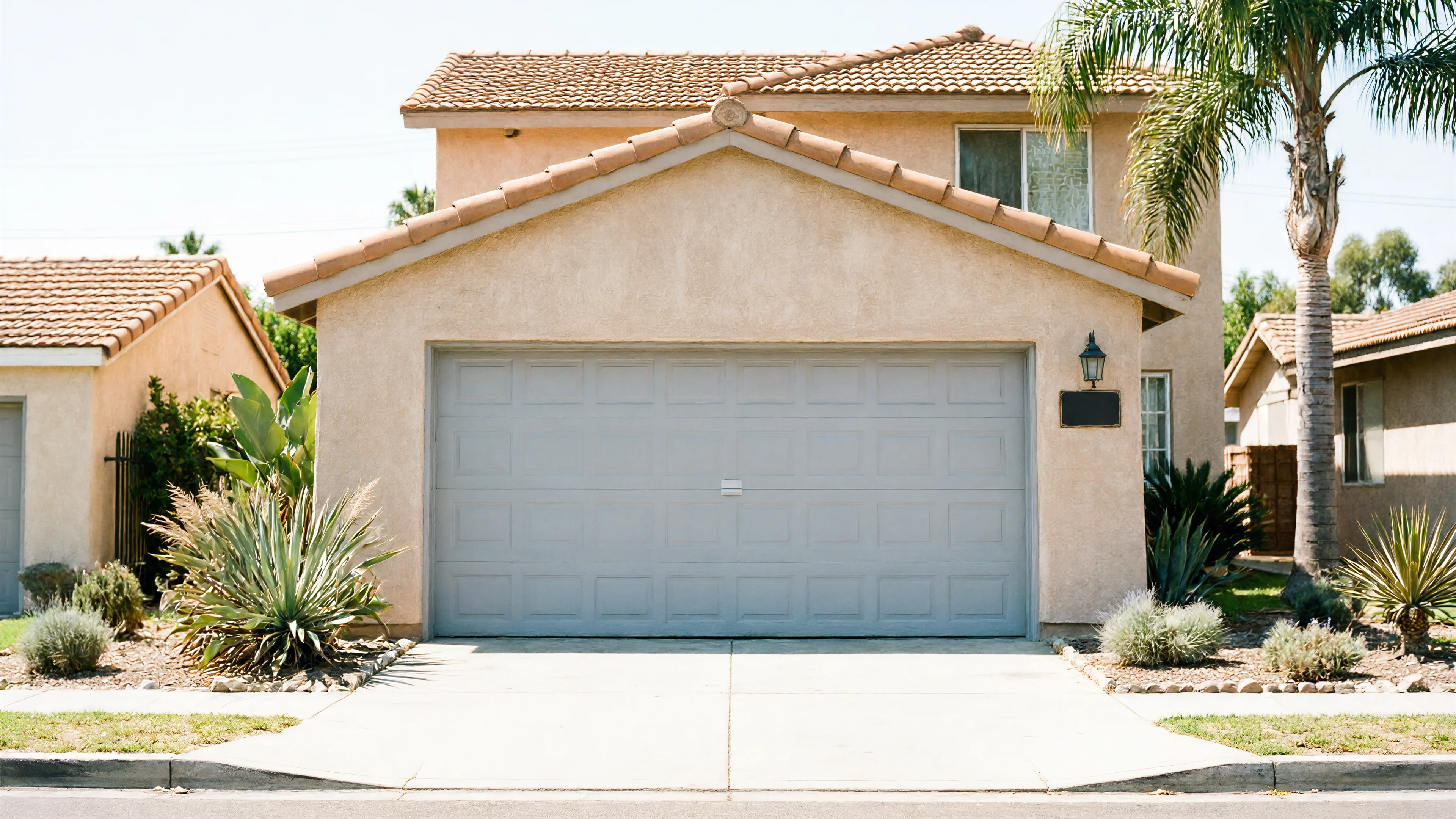 A light gray garage door on a tan house with a tiled roof.
